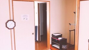 A traditional Japanese room with tatami flooring, a shoji screen door, a ceiling fan, and a small shelf with items.