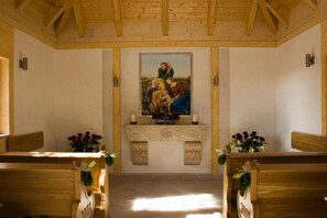 A church interior with wooden pews, a central altar with a painting, and floral decorations. - Hotel Haslbach FGZ (Regensburg)