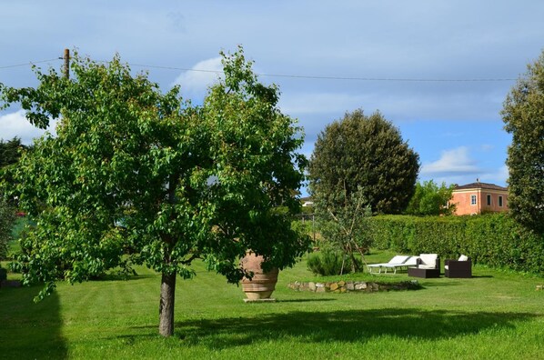 A well-maintained garden with a large tree, a stone planter, and a seating area with outdoor furniture. - Al Podere di Rosa (Lucca)