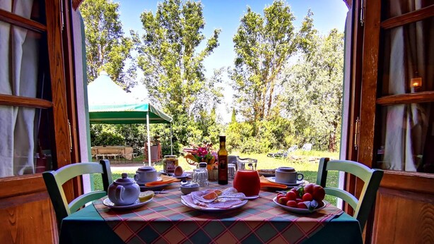 An outdoor dining area with a table set for breakfast, including plates, cups, and a bottle. - Al Podere di Rosa (Lucca)