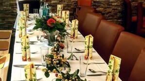 A long dining table set with folded napkins, clear glasses, cutlery, and decorative greenery. - Hotel Zur Sonne (Herrieden)