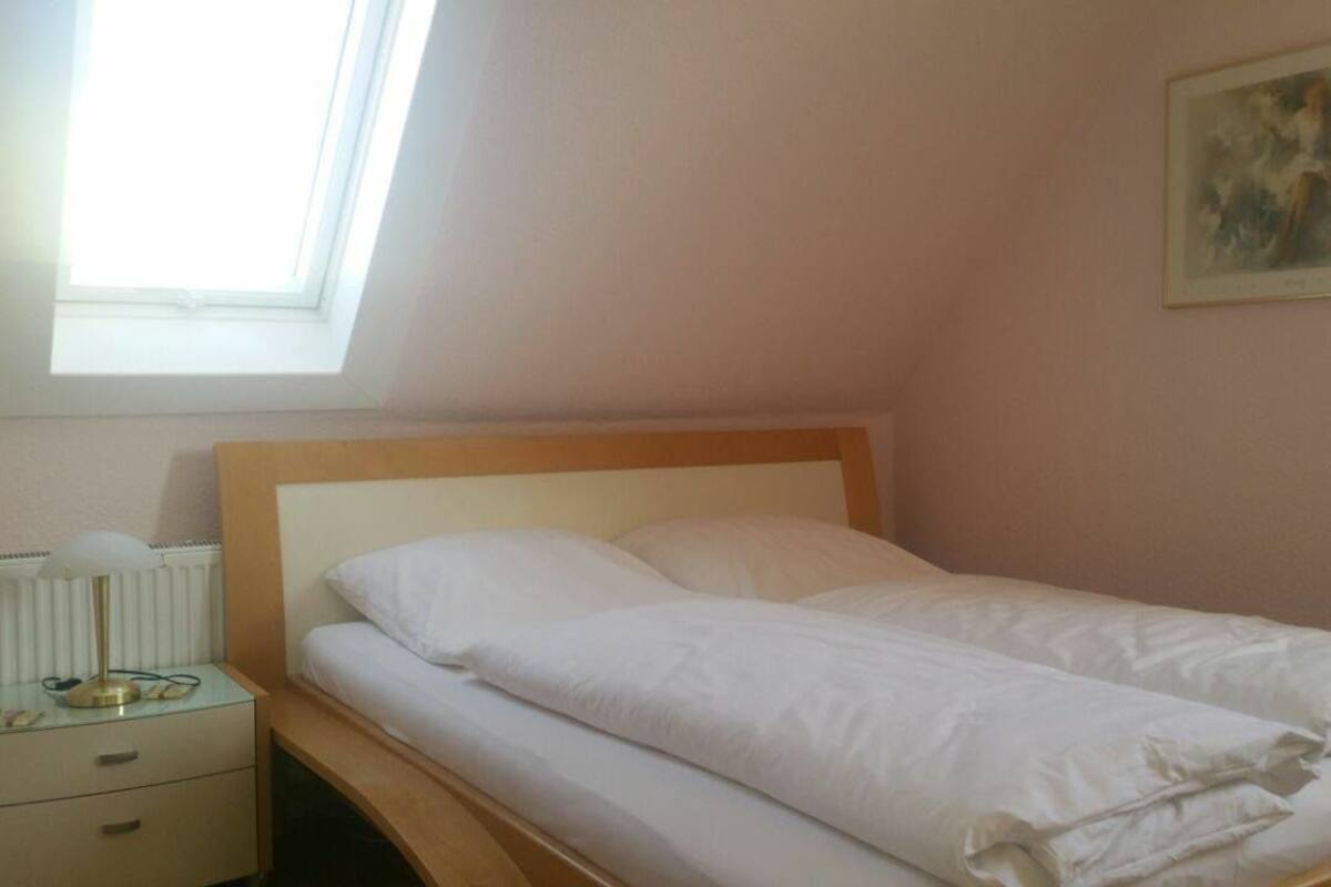 Un llit ben arropat amb roba de llit blanca a una habitació amb un fanal i un quadre al mur.