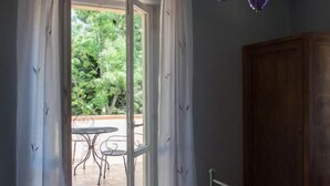 Un dormitorio con cama, un armario de madera, una lámpara de araña morada y vistas a un patio exterior con mesa y sillas.