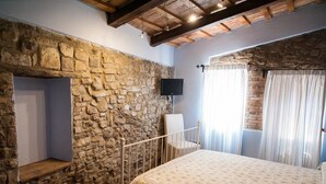 Un dormitorio con pared de piedra, cama, televisor montado en la pared y ventana con cortinas.