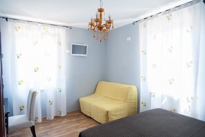 A bedroom with a bed, a yellow chair, a TV on the wall, and a chandelier. - Agriturismo La Solagna (Montebello di Bertona)