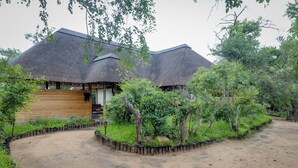 A thatched-roof building with a wooden exterior, surrounded by a landscaped garden with various plants and trees. - Tangala Safari Camp (Hoedspruit)