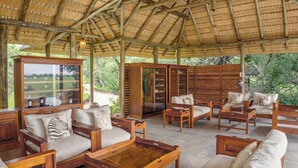 A covered outdoor seating area with wooden furniture and a glass cabinet. - Tangala Safari Camp (Hoedspruit)