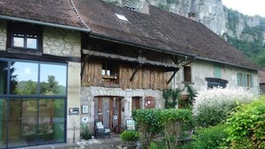 Un edificio rústico de piedra con un balcón de madera, un acceso de vidrio y un camino de jardín que lleva a la puerta.