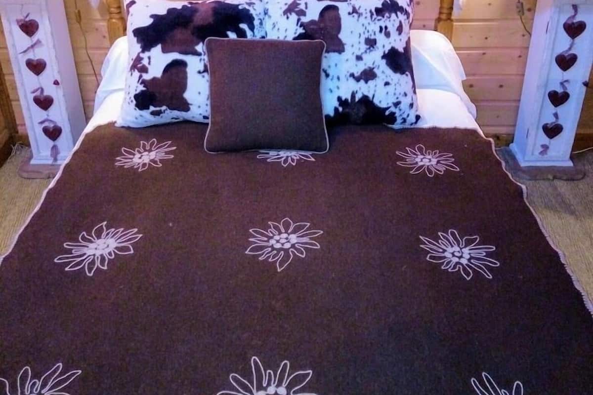 Un dormitorio estilo cabaña de madera con cama, decoración de corazón en la pared y lámparas con forma de corazón en las mesitas de noche.