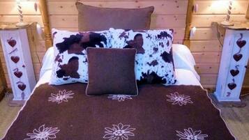 A wooden cabin-style bedroom with a bed, heart-shaped wall decoration, and heart-shaped lampshades on nightstands.