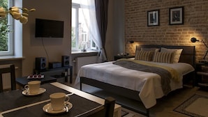 A hotel room with a bed, a TV, a dining table with two cups, and a brick wall. - Apartamenty 2M (Czestochowa)