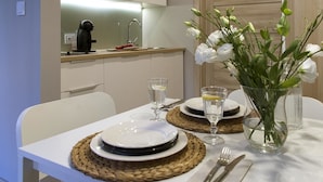 A dining table set with plates, cutlery, and glasses, with a vase of flowers and a coffee machine in the background. - Apartamenty 2M (Czestochowa)