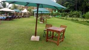 An outdoor seating area with wooden tables and chairs, green umbrellas, and a pool in the background. - Sun Set Paradise Baringo (Mombasa)