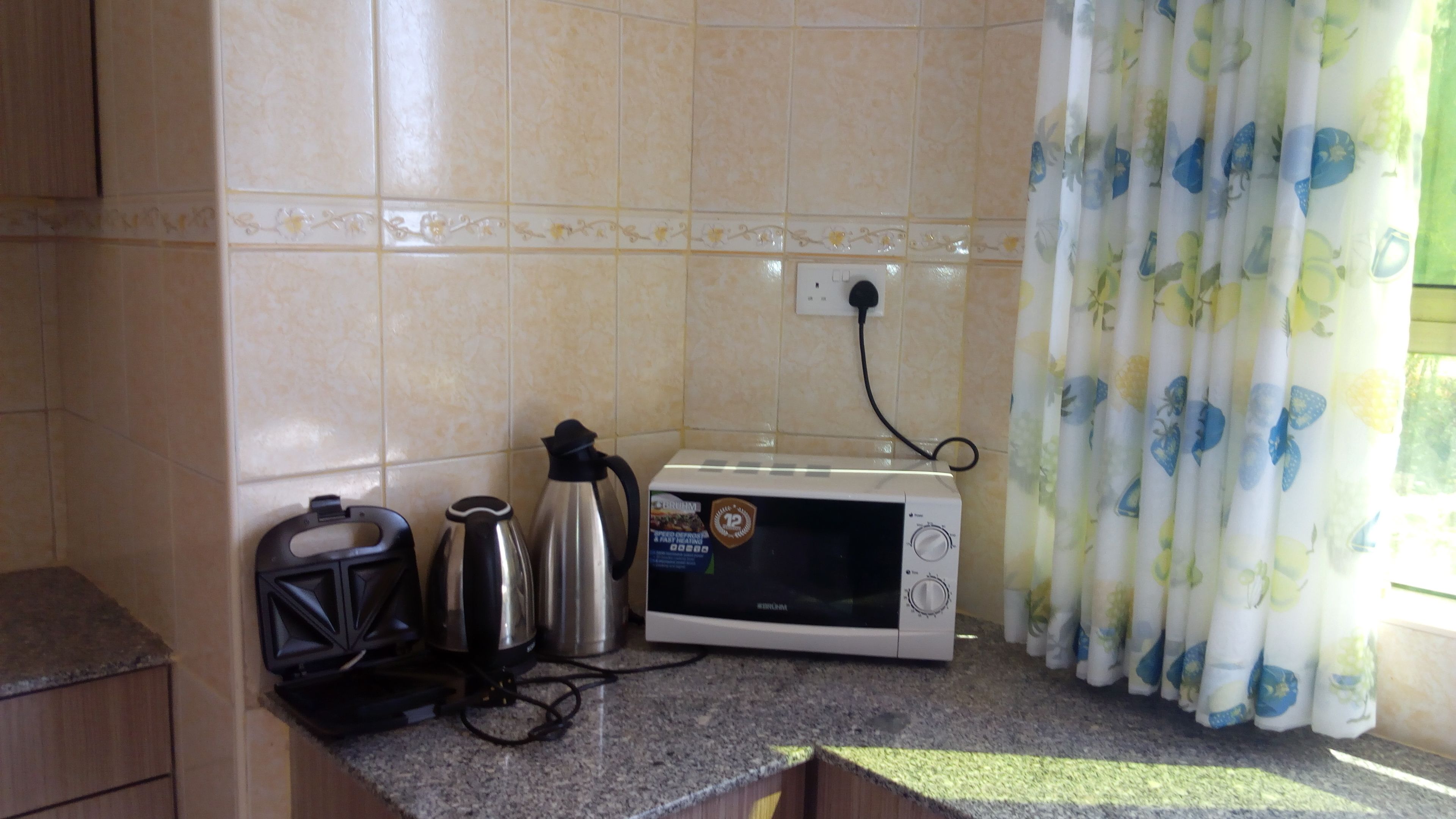 Uma cozinha com micro-ondas, chaleira e torradeira em bancada de granito.