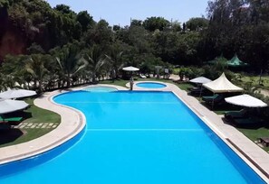 A swimming pool with a curved design, surrounded by palm trees and green umbrellas. - Sun Set Paradise Baringo (Mombasa)