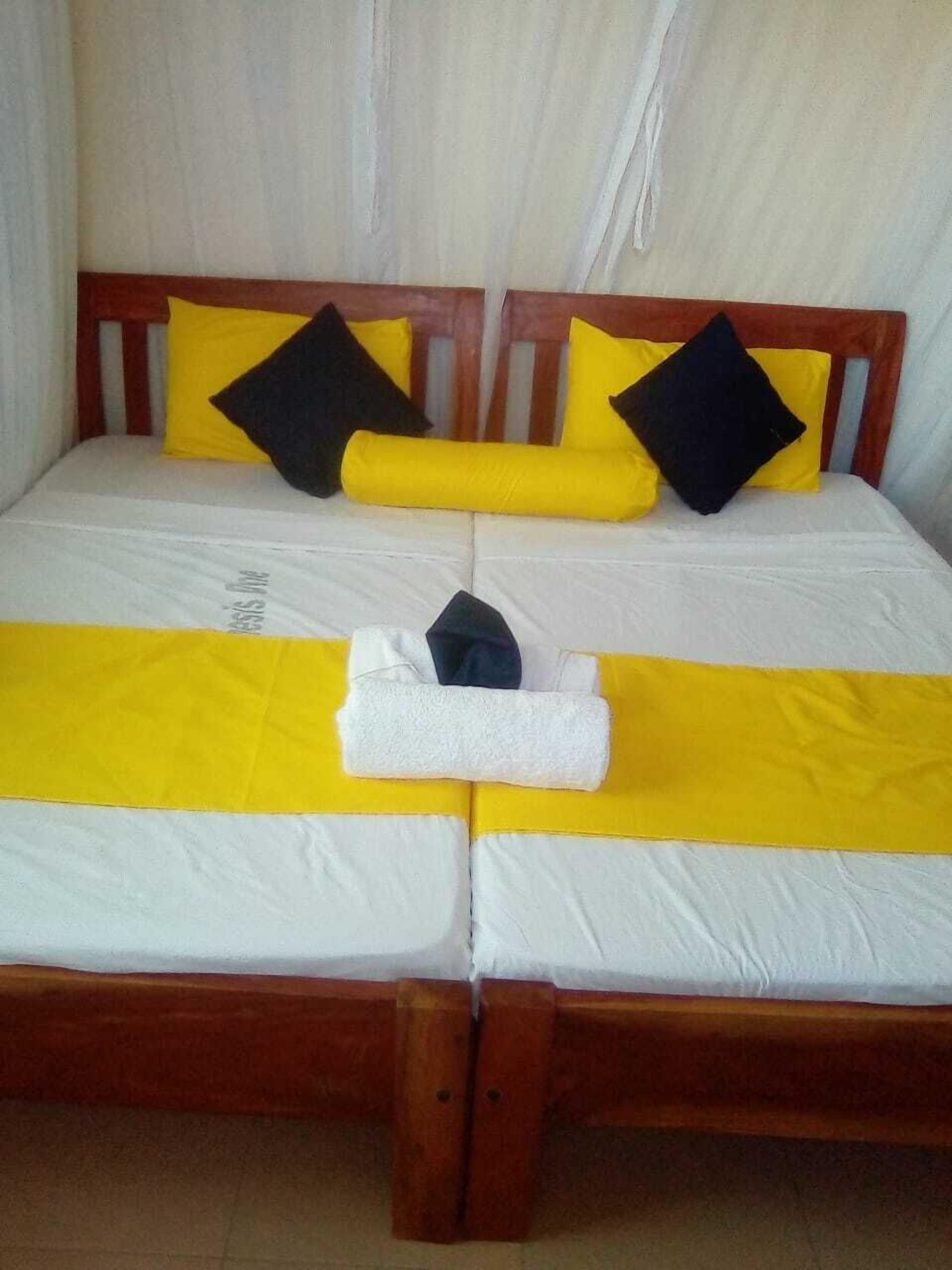 Ein Bett mit Holzrahmen, Bettwäsche in Weiß und Gelb sowie zwei schwarze Kissen.