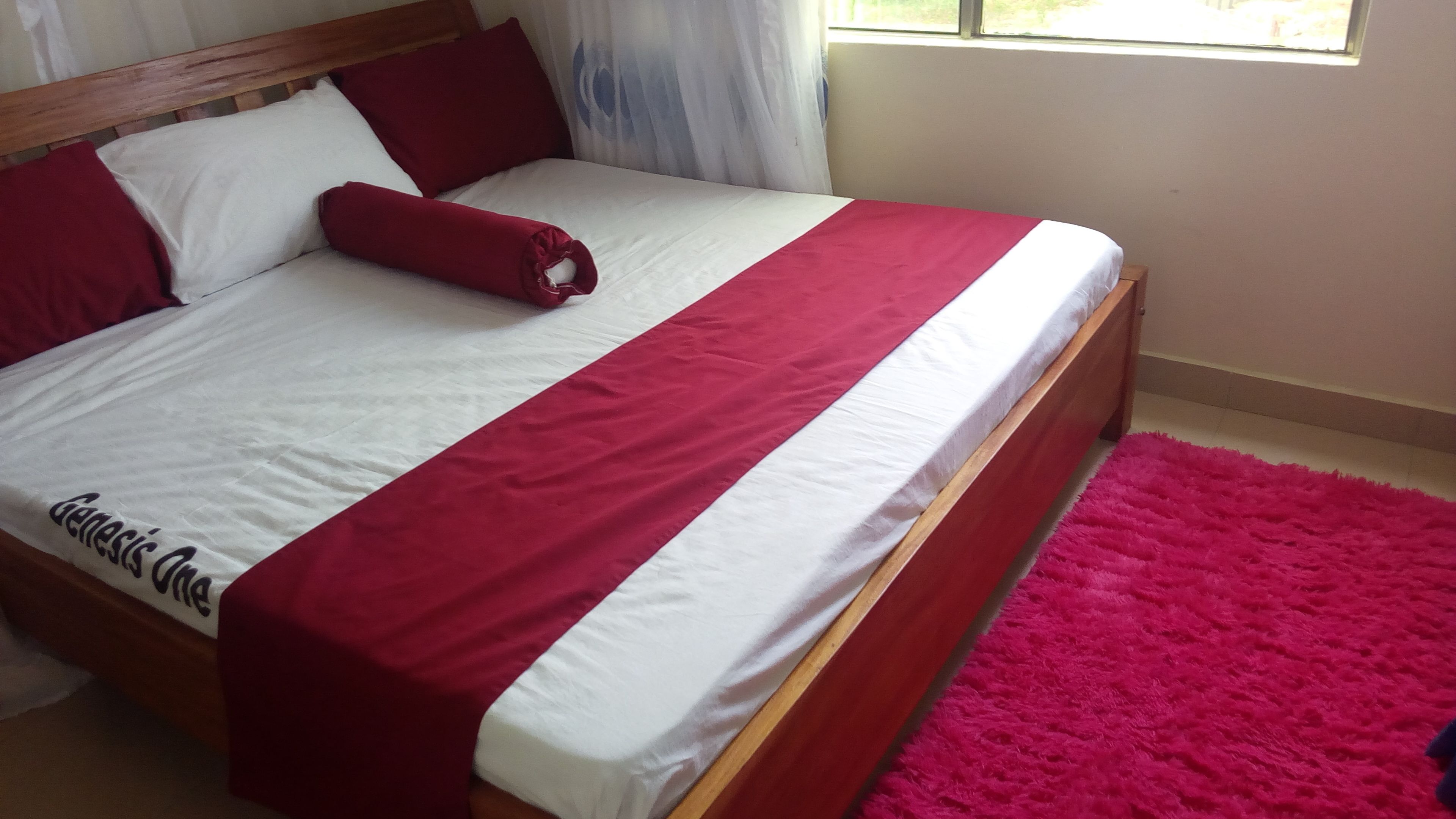 A bed with a wooden frame, white and red bedding, and a pink rug.