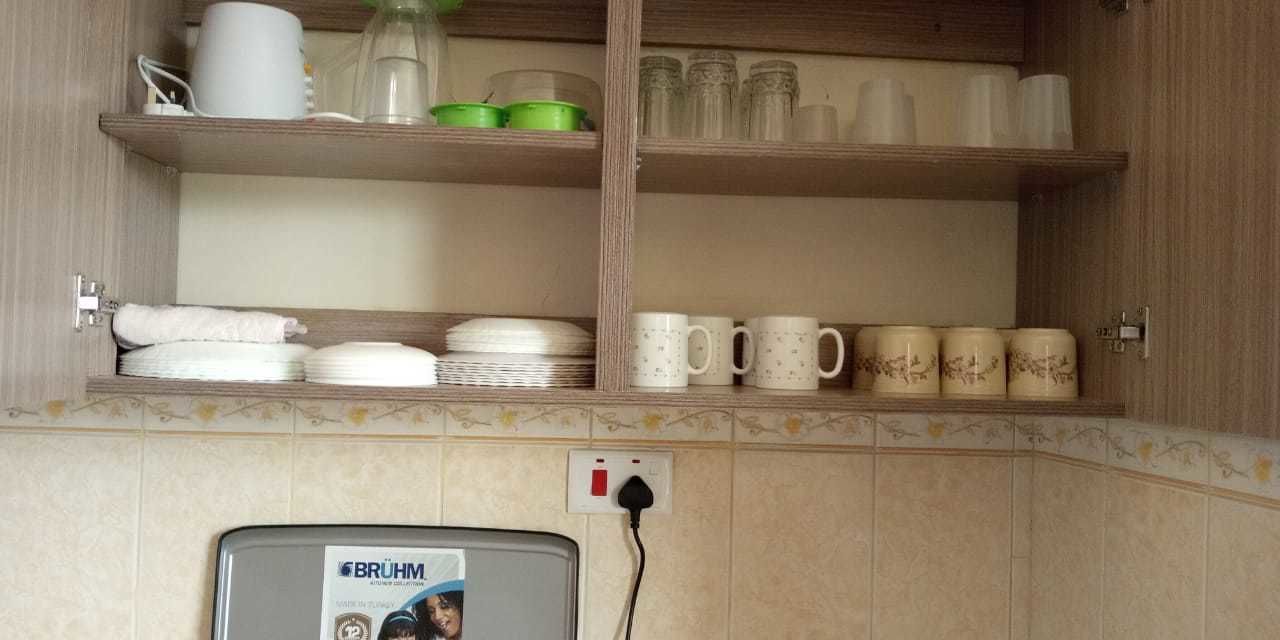 A kitchen with shelves holding plates, bowls, and mugs. There is a power outlet and a Brummel TV on the counter.