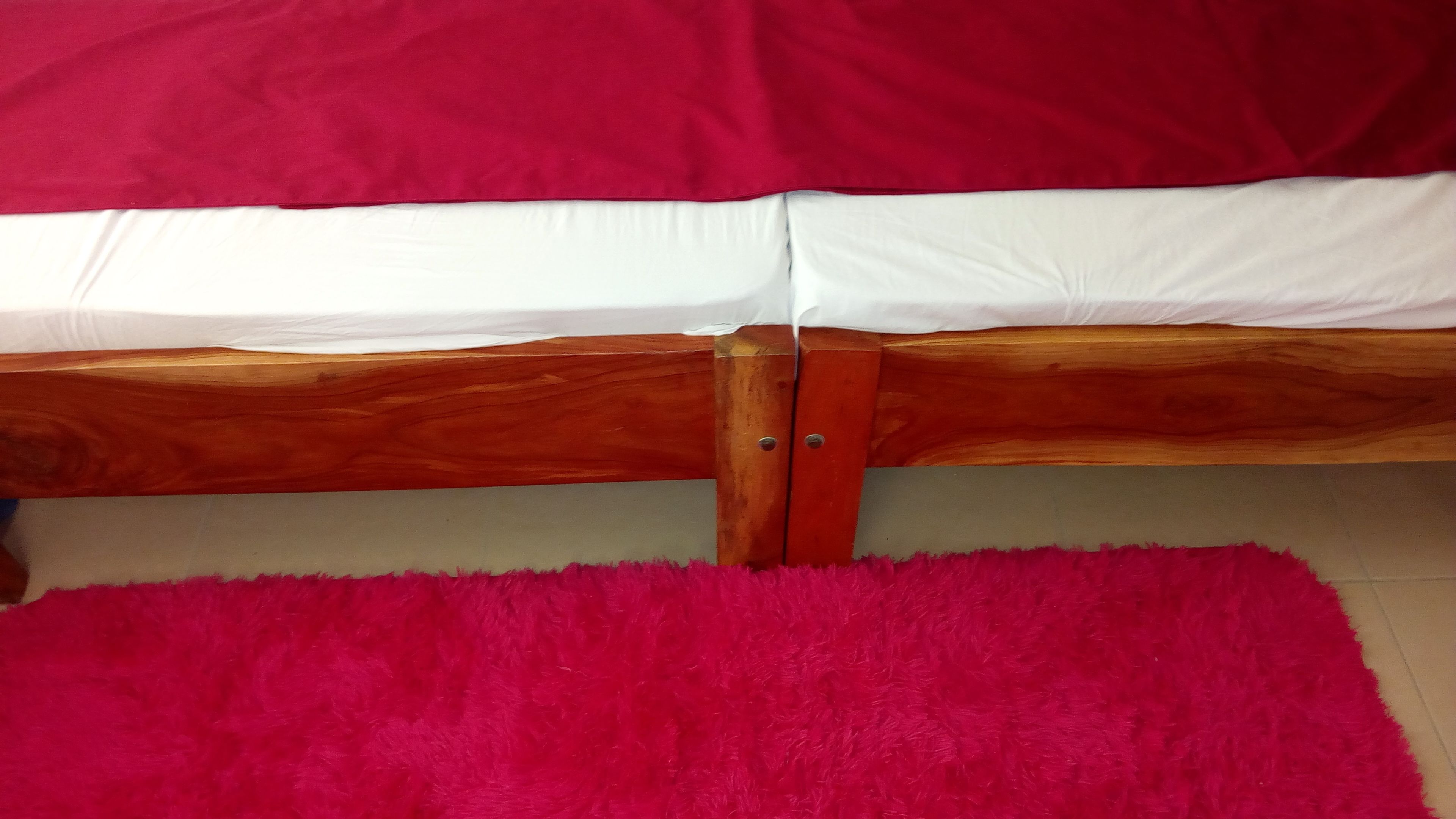 A bed with a wooden frame, white bedding, and a red pillow.