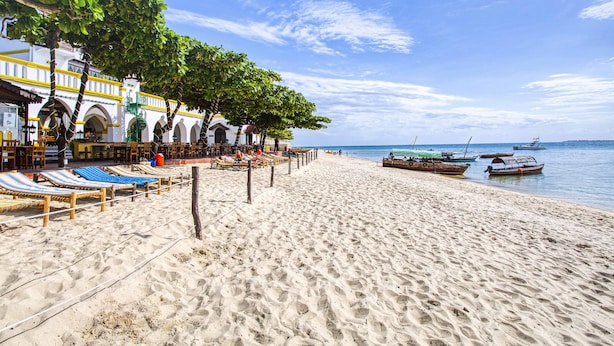 Una spiaggia con lettini e un ristorante con tavoli all'aperto.