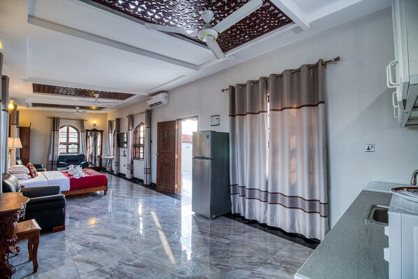A hotel room with a bed, a desk, a chair, a refrigerator, and a bathroom with a shower.