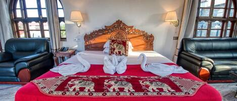 A hotel room with a large bed, two black leather armchairs, a wooden headboard, and a red bedspread with a decorative pattern.