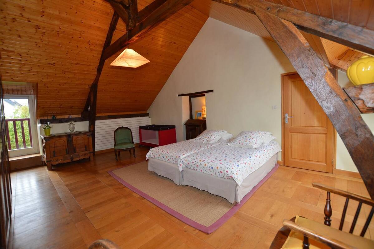 A cozy attic bedroom with a sloped ceiling, a bed with floral bedding, a chair, a small table, and a window with a view.
