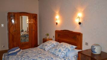 A bedroom with a wooden bed, a wardrobe, two wall-mounted lamps, and a small bedside table with a vase.