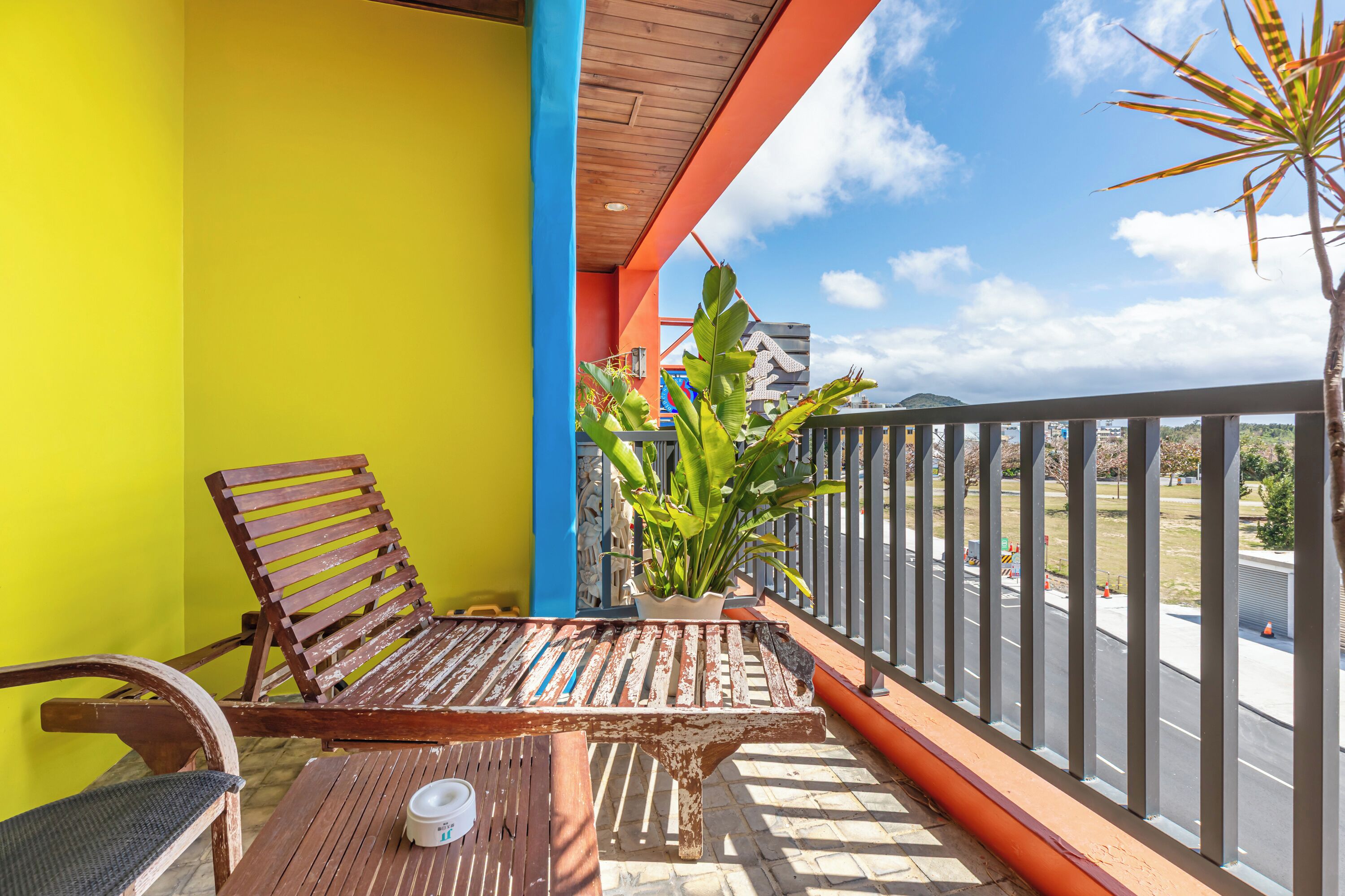 A balcony with a wooden bench, a potted plant, and a view of a road and distant landscape.