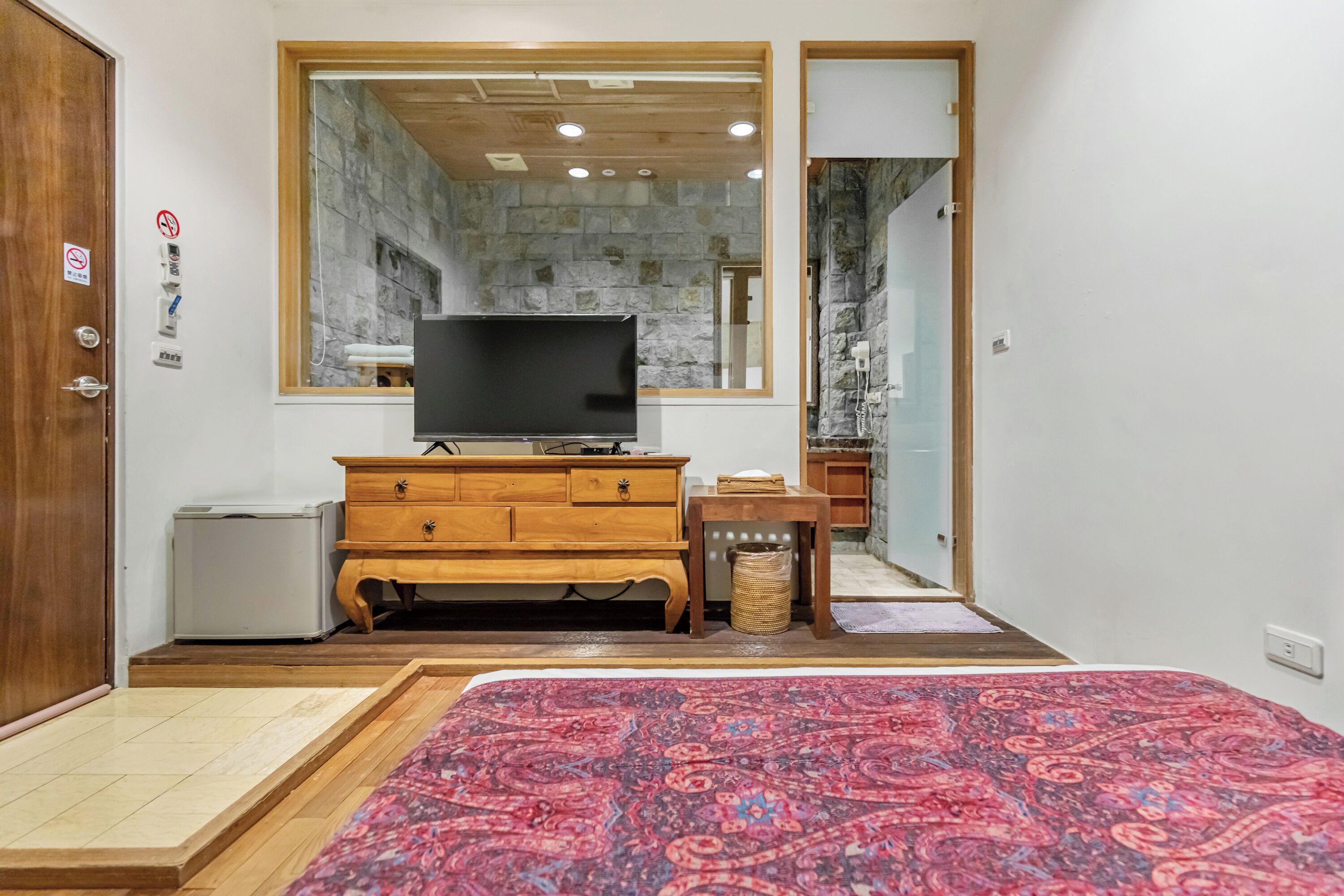 Un dormitorio con una cama grande, un aparador de madera, un televisor y una pared de piedra.