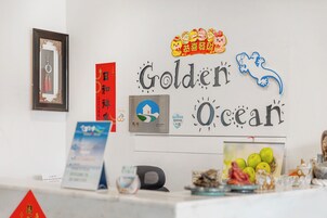 Una mesa de recepción con un cartel que dice "Golden Ocean". Hay varios objetos sobre la mesa, como un cuenco de manzanas, un reloj y algunos adornos.