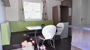 A compact room with a green sofa, a small table, a white chair, and a kitchenette area.