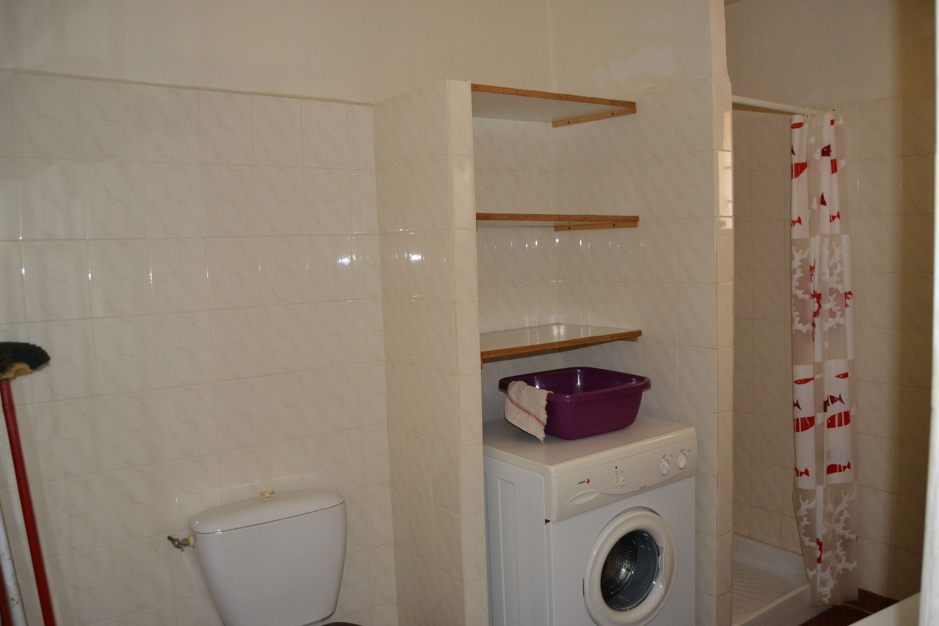 A bathroom with a toilet, washing machine, and shelves.