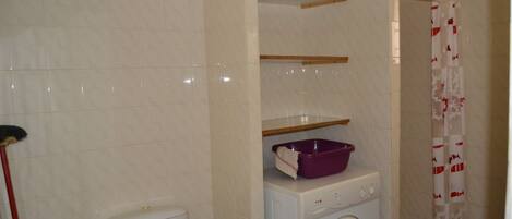 A bathroom with a toilet, washing machine, and shelves.