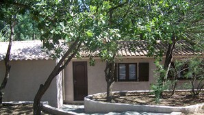 A small building with a tiled roof, a door, and a window. There are trees and shrubs around the building.