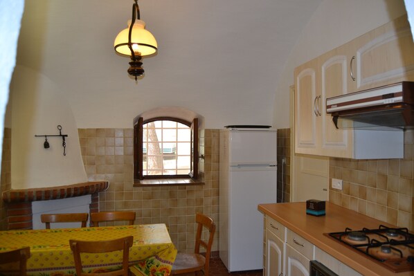 A compact kitchen with a dining area, featuring a gas stove, a refrigerator, and a window with a view.