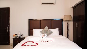 Un lit bien fait, avec du linge de lit blanc, un coussin décoratif et une composition en forme de cœur faite de serviettes et de pétales de rose.