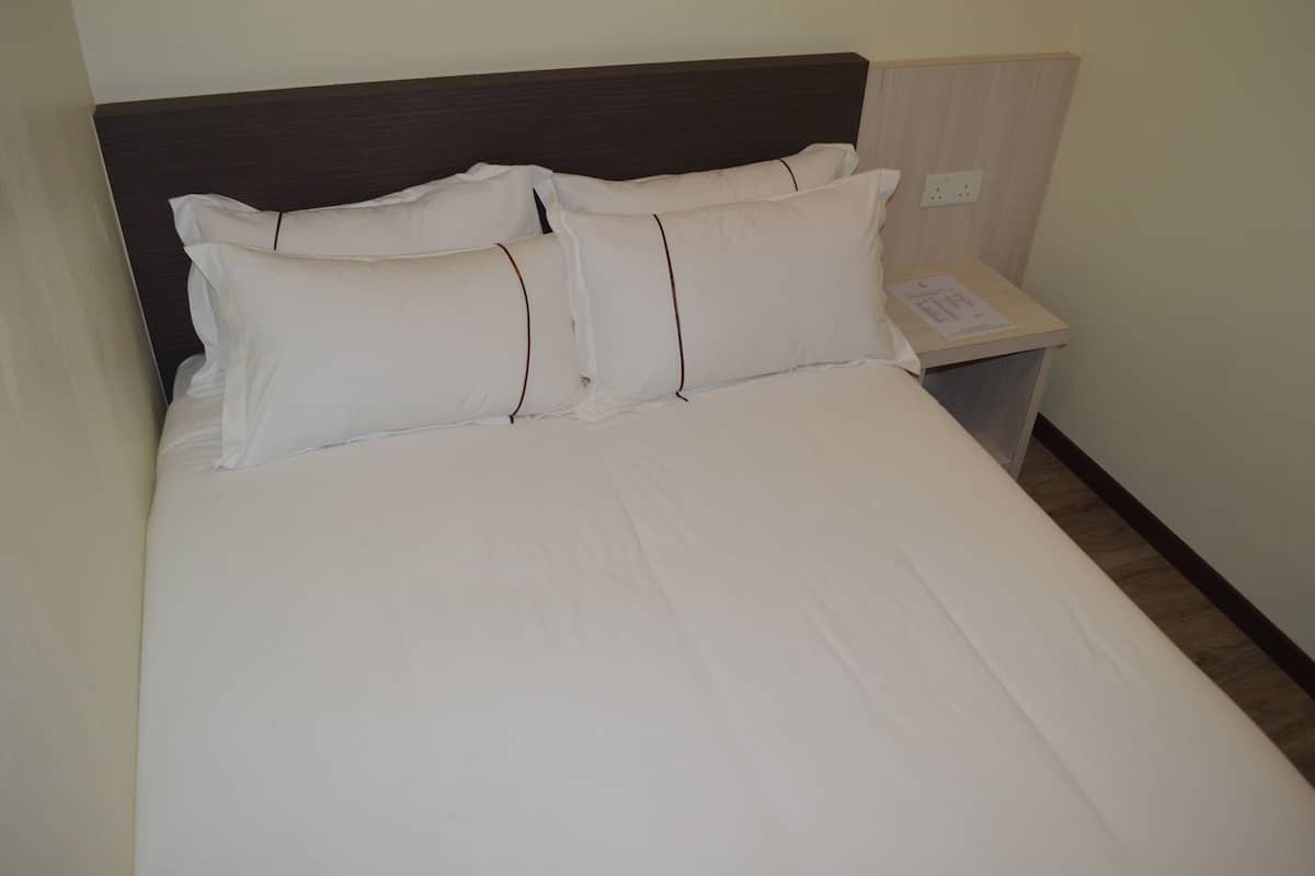 A neatly made bed with white linens and pillows, a wooden headboard, and a small bedside table with a lamp.