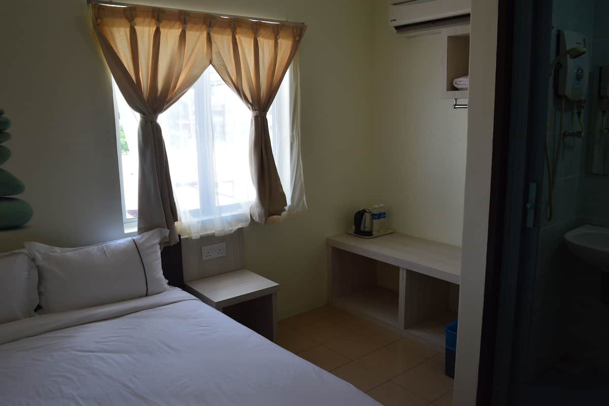 A hotel room with a bed, a nightstand, a small table with a bottle and a cup, and a window with curtains.
