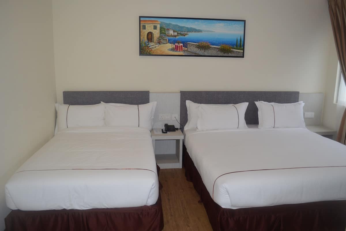 A hotel room with two beds, a nightstand with a phone, and a painting of a coastal scene on the wall.