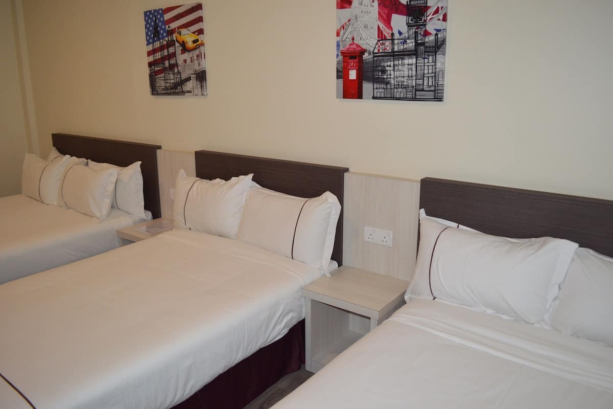 A hotel room with three single beds, each with white bedding and a wooden headboard. There are two small bedside tables with lamps.