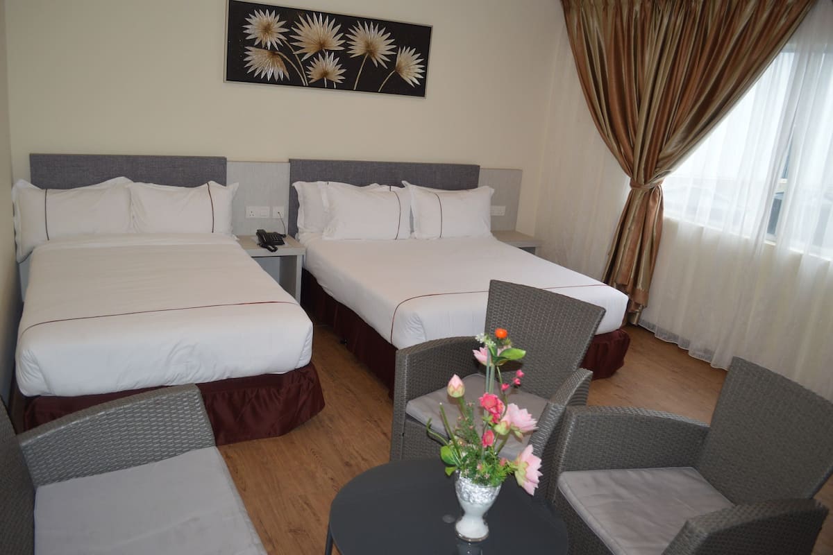 A hotel room with two beds, a small table with a vase of flowers, and a chair.