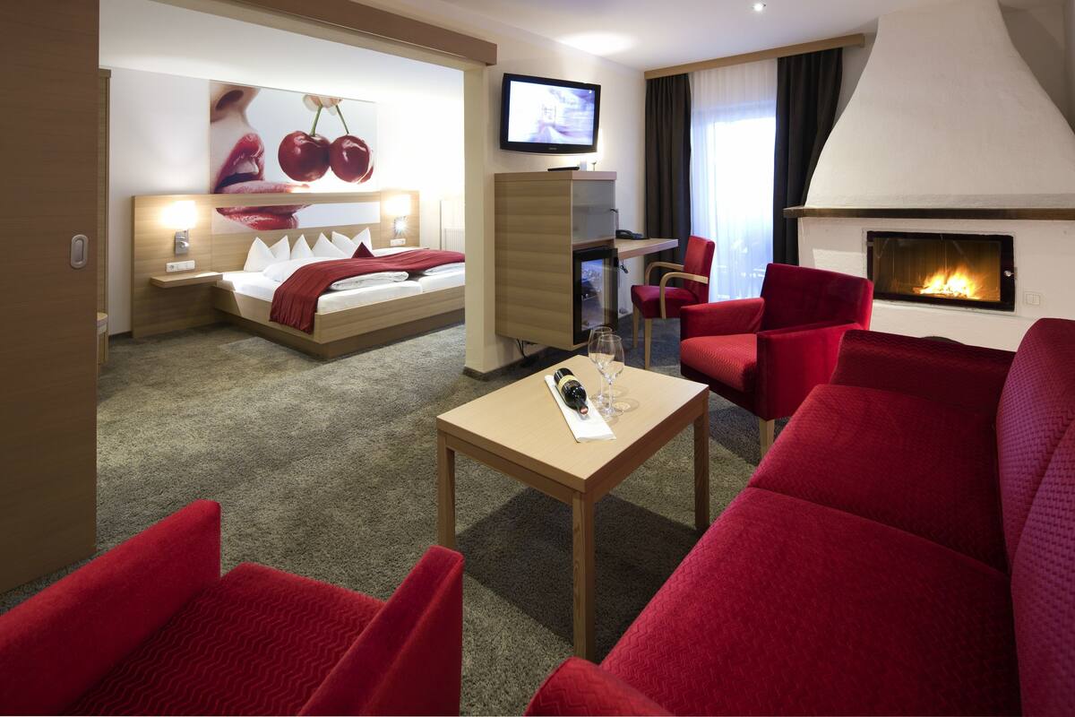A hotel room with a bed, a TV, a fireplace, red furniture, and a carpeted floor.