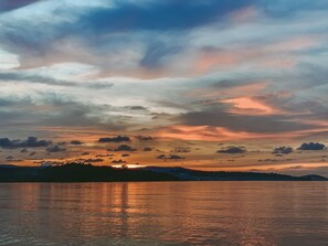 A sunset over a calm body of water with a silhouette of a distant landmass. - Ariya Resort (Koh Rong)