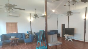 A spacious living room with a blue sofa set, a wooden floor, and ceiling fans. - Ariya Resort (Koh Rong)