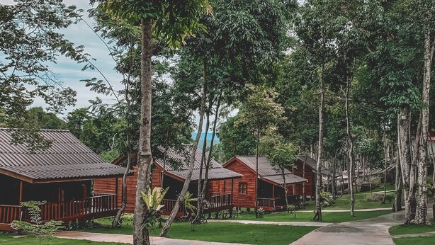 A row of wooden cabins with metal roofs, surrounded by tall trees and a well-maintained lawn. - Ariya Resort (Koh Rong)