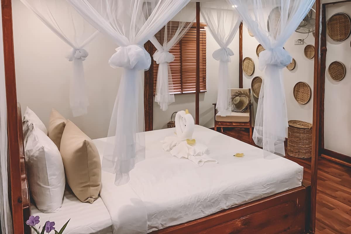 A neatly made bed with white linens, a canopy, and decorative pillows.