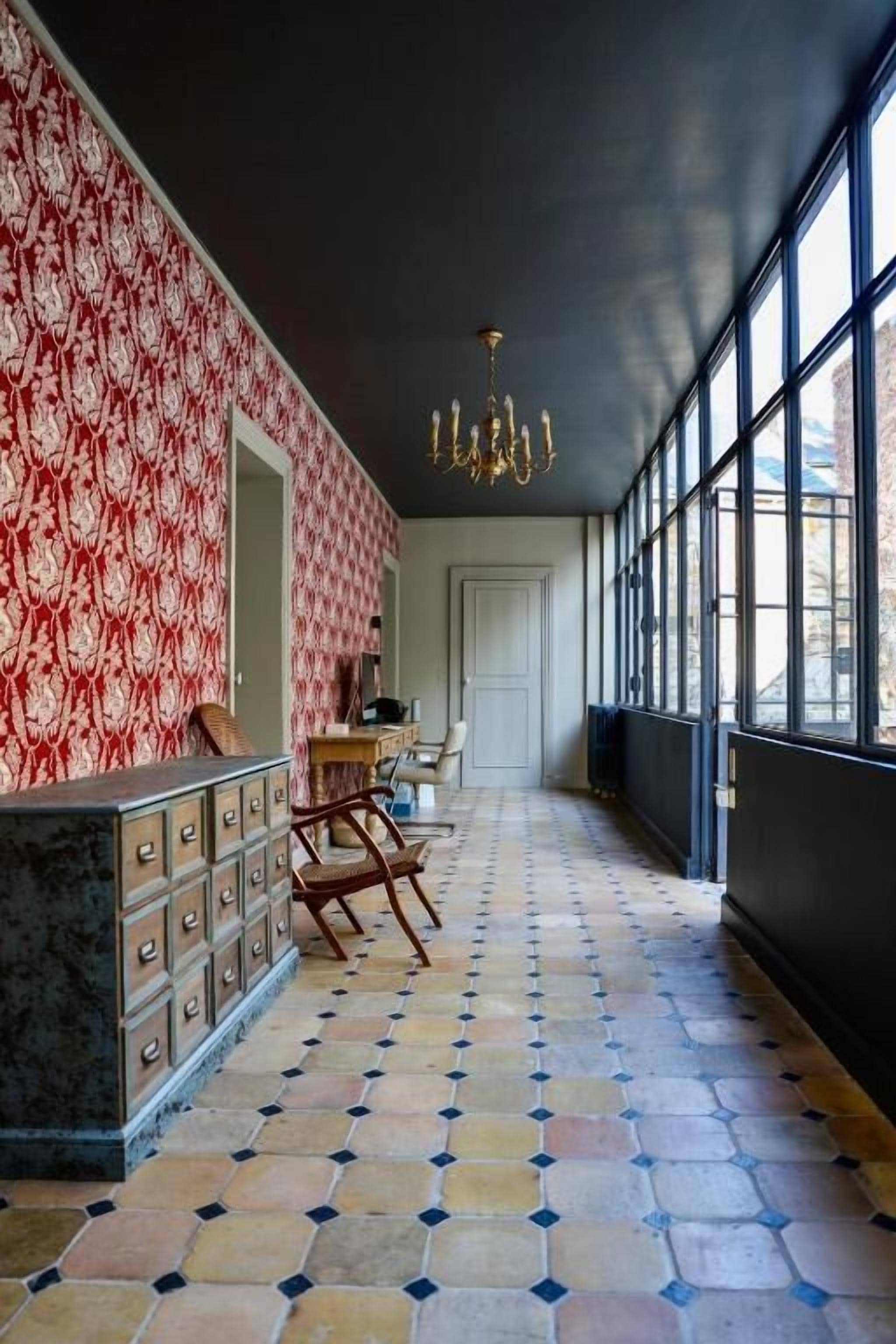 A hallway with patterned wallpaper, a chandelier, and a tiled floor.