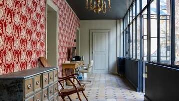 A hallway with patterned wallpaper, a chandelier, and a tiled floor.