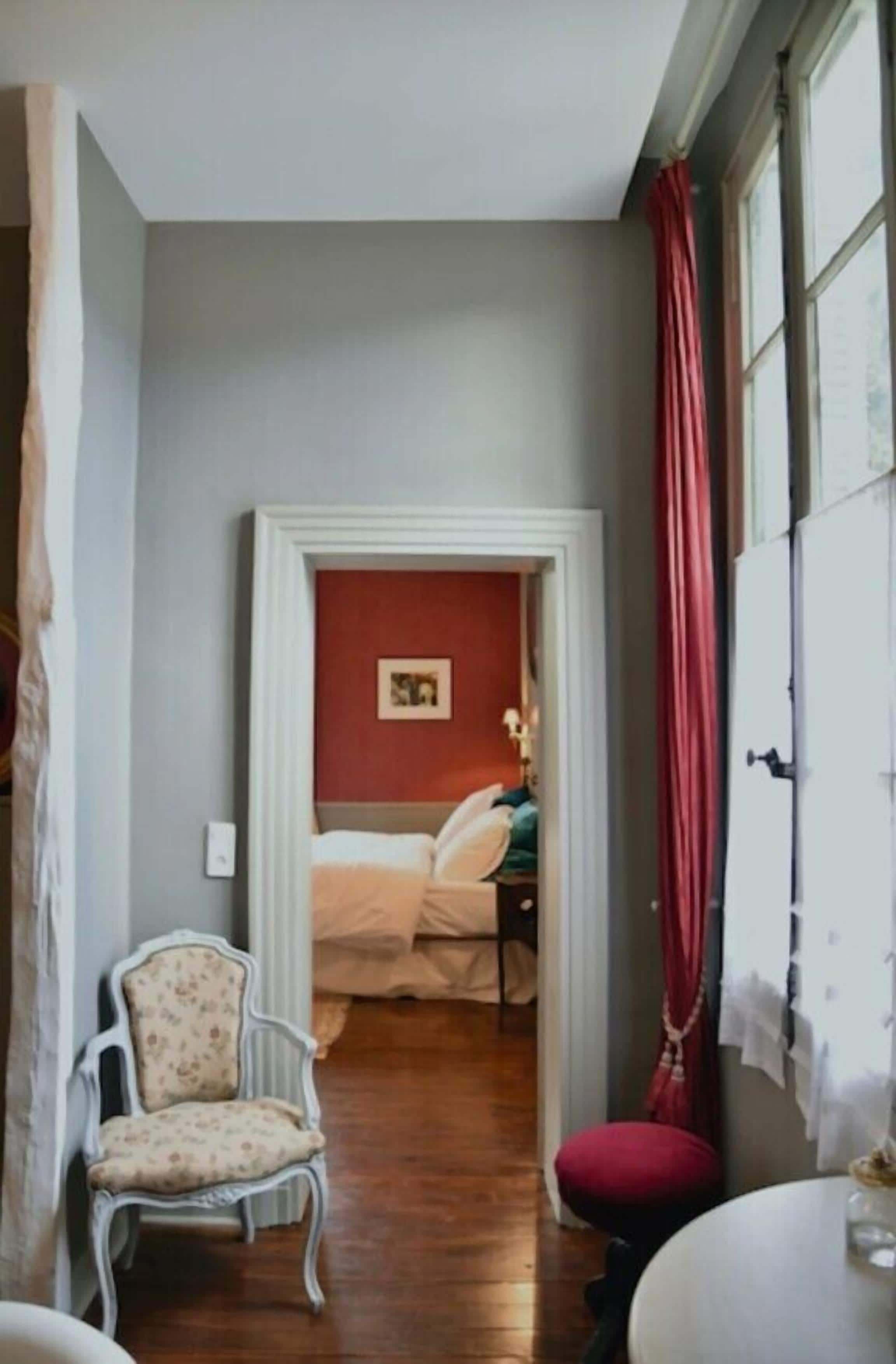 Een kamer met een bed, een stoel, een tafel en een raam met gordijnen.
